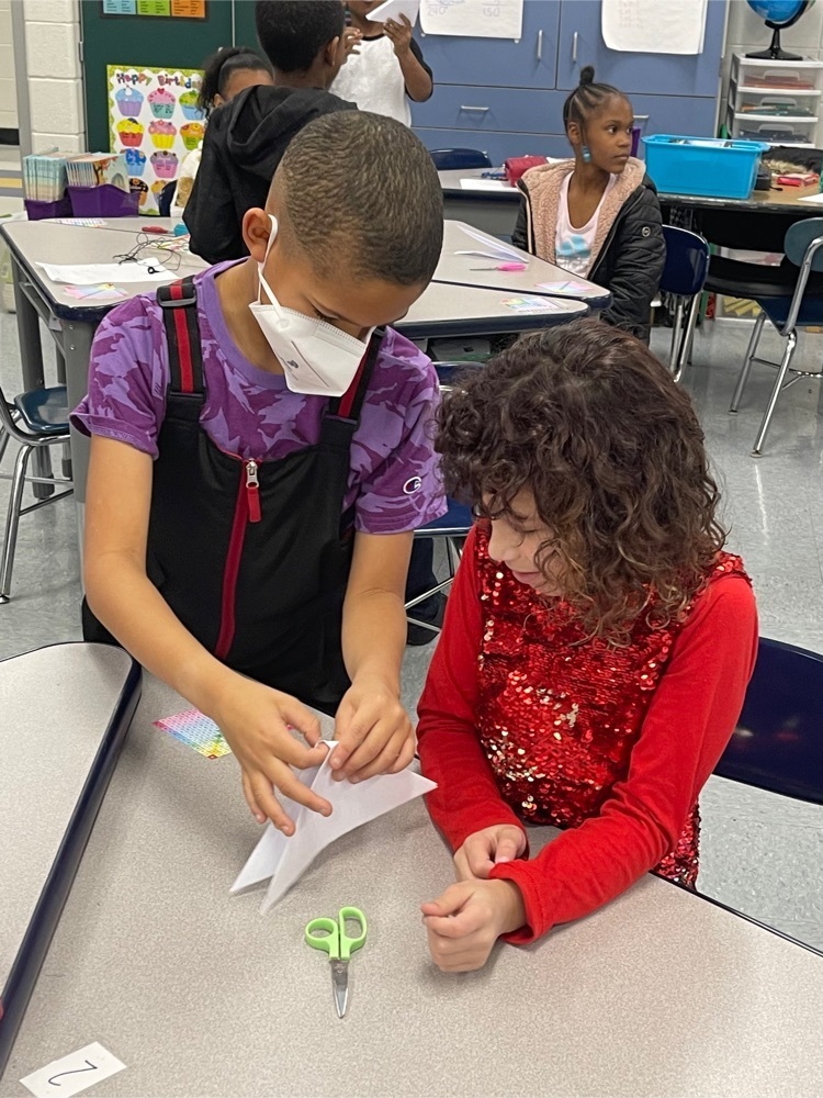 Third grade student teaching a peer how to make a snowflake 